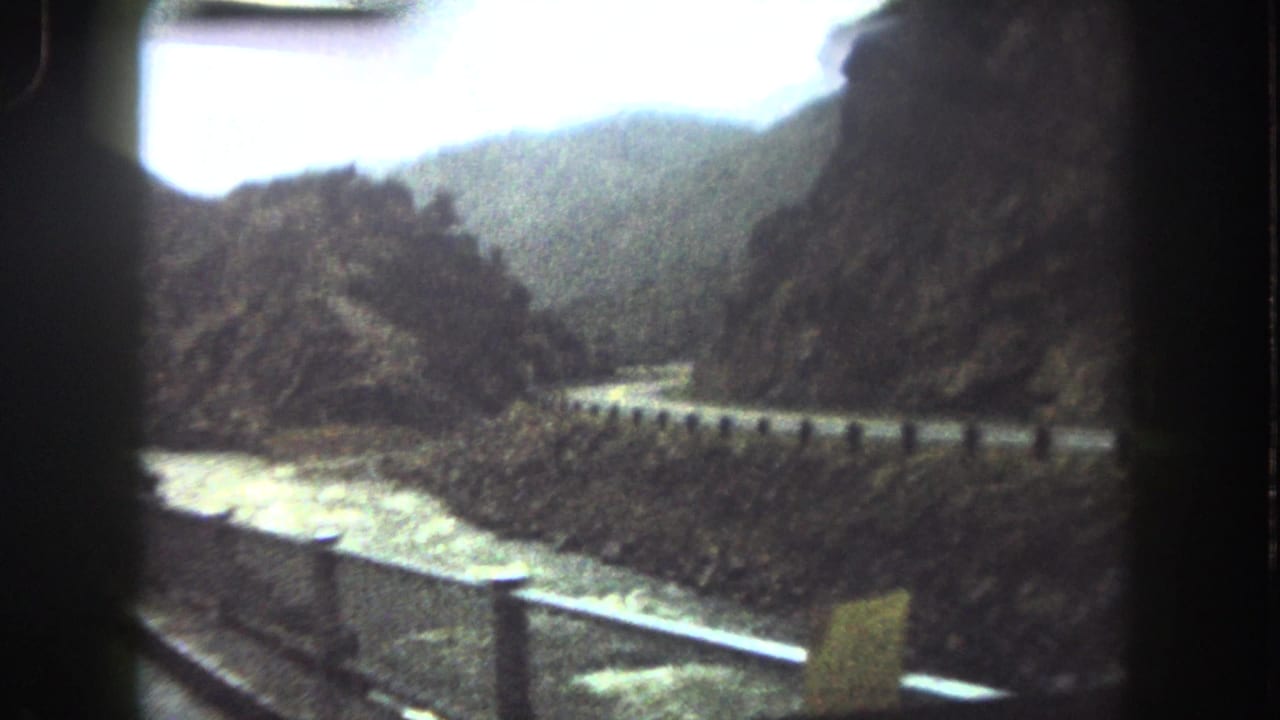Curving roadside guardrail above a river in a narrow mountain valley.