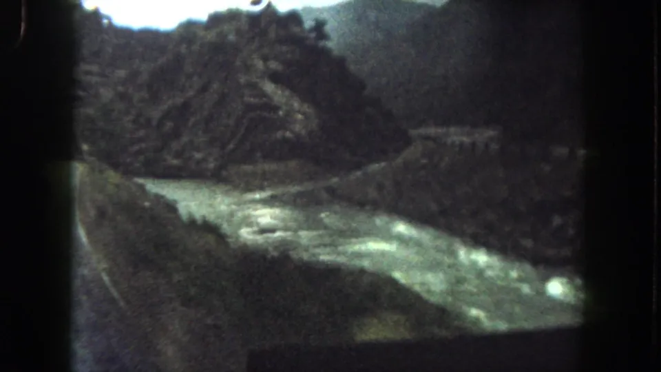 Summit County home-movie frame with a river, roadside guardrail, rocky outcrop and dark mountain wall.