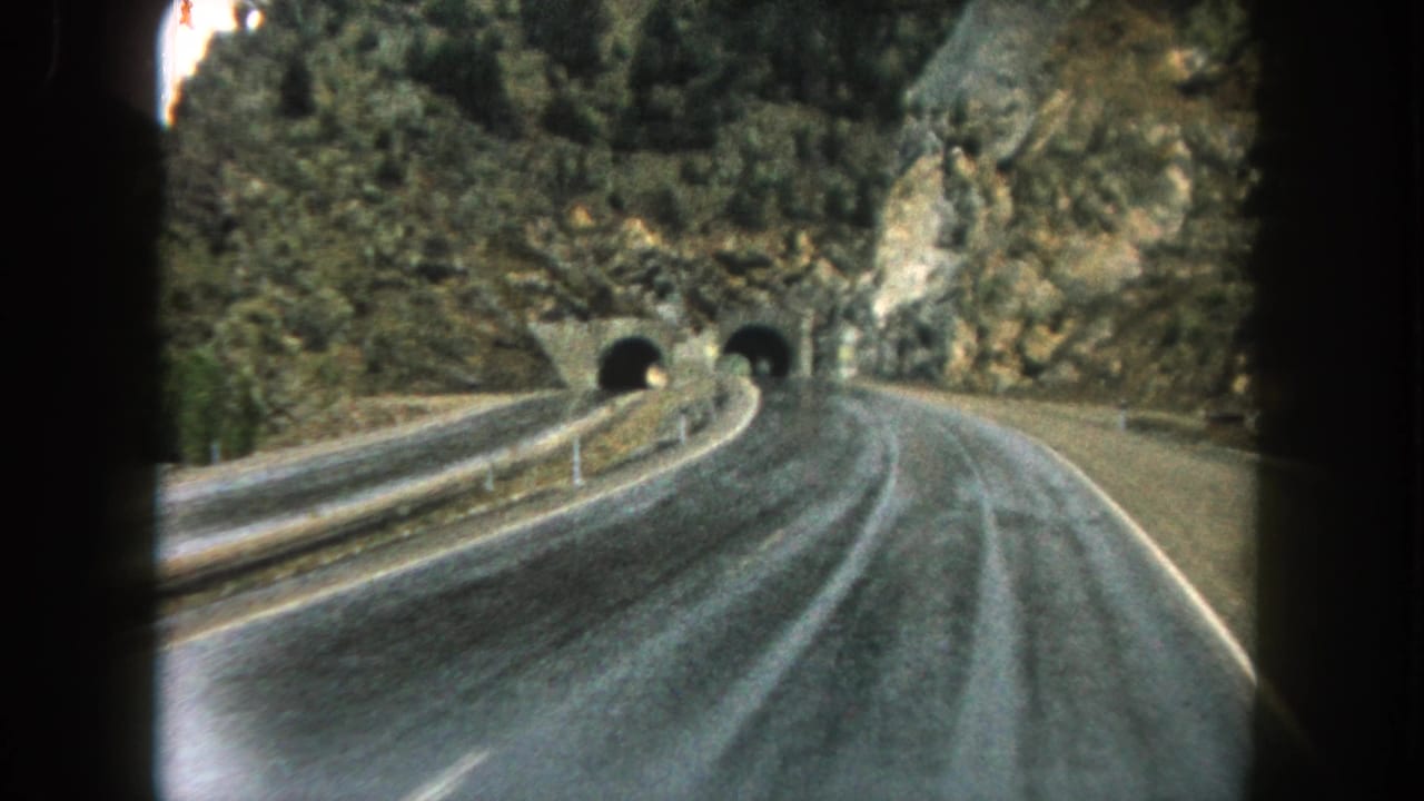 Moving 8mm road view in Summit County, Colorado, with guardrails leading toward two dark mountain tunnel entrances.