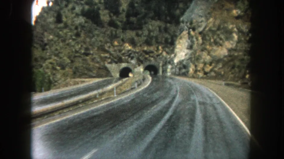 Moving 8mm road view in Summit County, Colorado, with guardrails leading toward two dark mountain tunnel entrances.