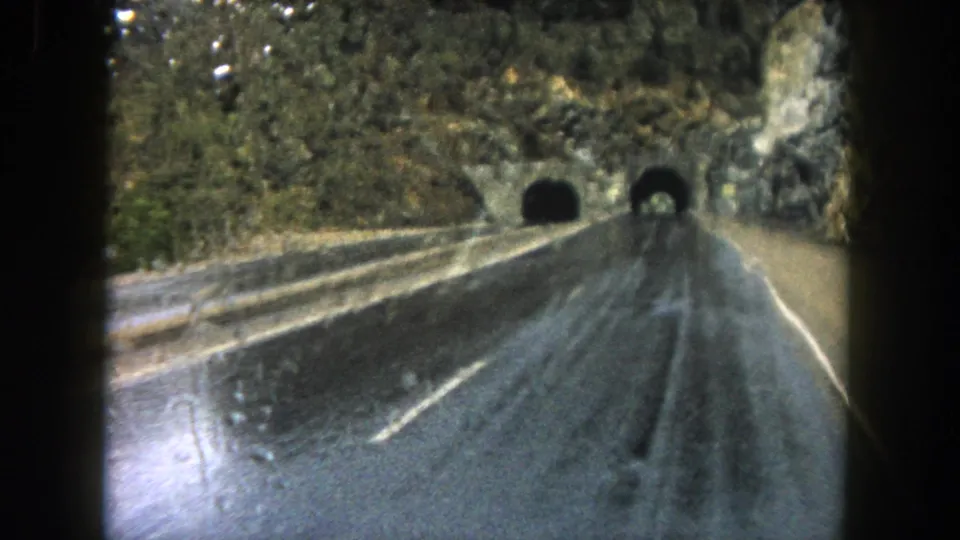 Passenger-view 8mm frame from Summit County, Colorado, with rain on the glass and a wet highway leading into mountain tunnels.