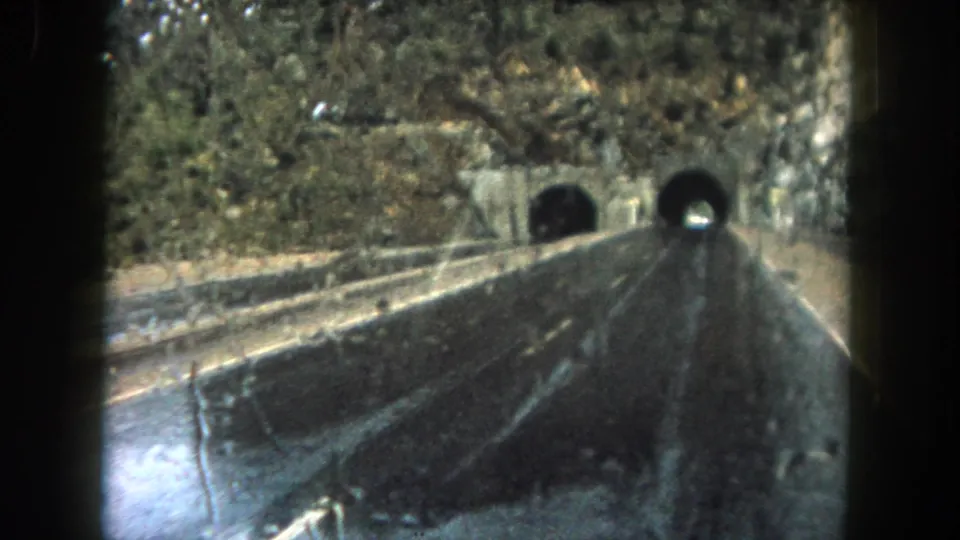 Late frame of the 1962 Summit County road scene, showing rain on the window, wet pavement, and tunnel openings ahead in the rock.
