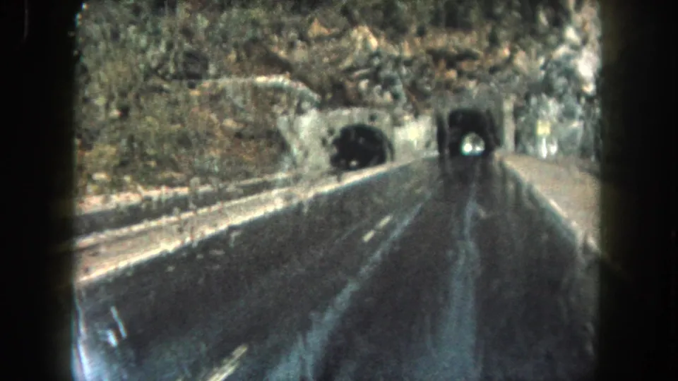 Vehicle-perspective 8mm frame from Summit County, Colorado, with wet pavement and a tunnel entrance ahead.