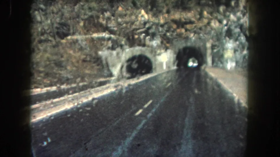 1962 Colorado home-movie frame showing the car nearing tunnel portals along a rain-darkened highway.