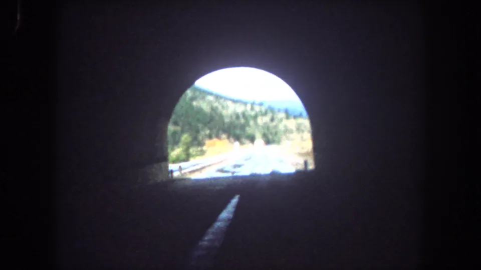 1962 8mm view from inside a Summit County, Colorado tunnel, looking toward daylight and a wet mountain road outside.