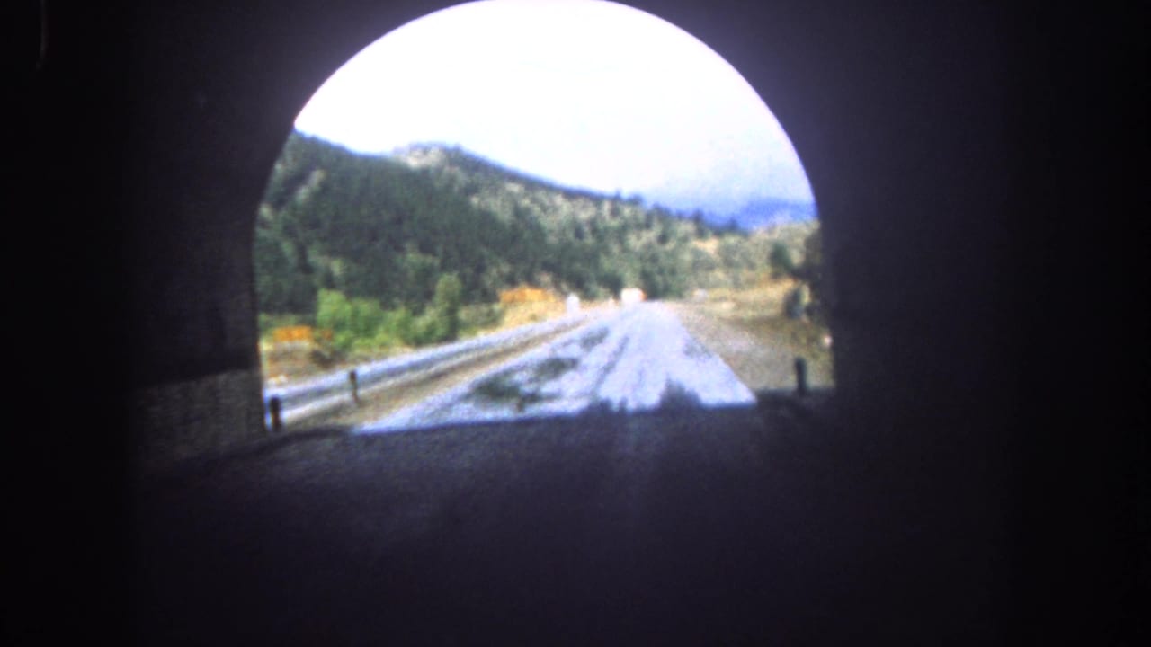 View near a tunnel exit with a wet road leading into wooded hills.