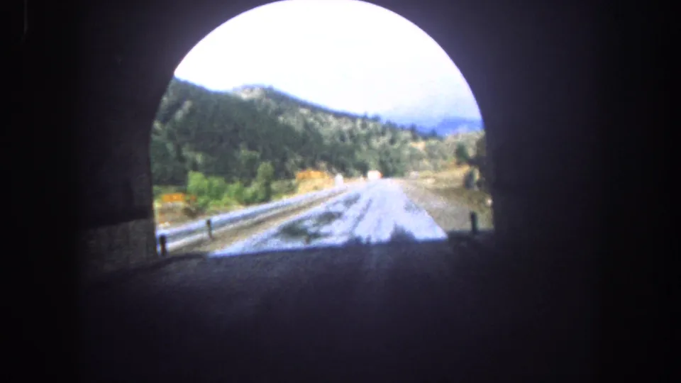 Driver’s-view 8mm frame emerging from a Colorado tunnel onto a wet road bordered by guardrail and hills.