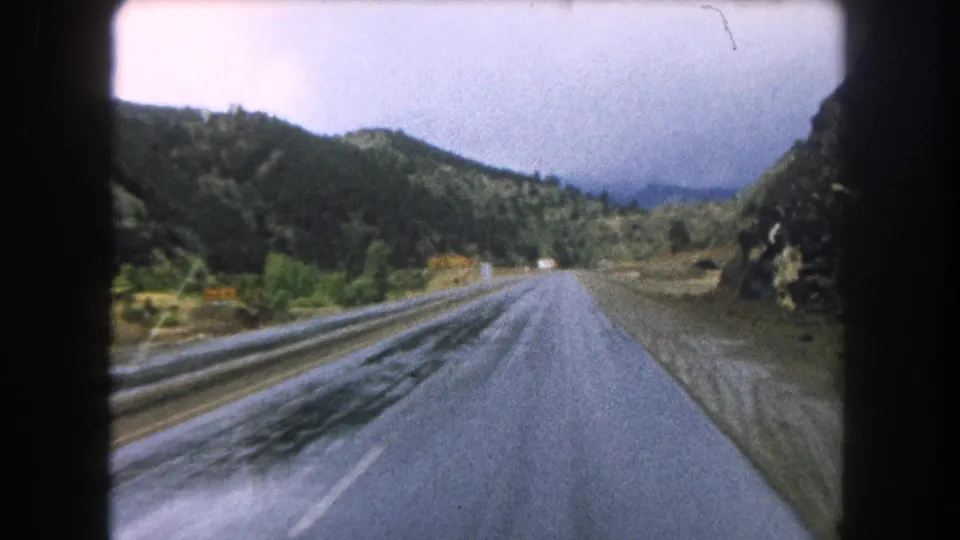 Summit County, Colorado road-view frame from 1962 8mm footage, showing wet pavement, hills, and the tunnel edge behind the camera path.