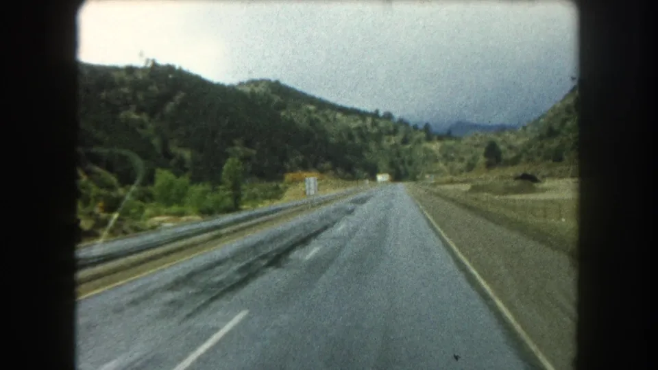 Final 1962 8mm frame of a damp Summit County road receding toward wooded slopes and low clouds.