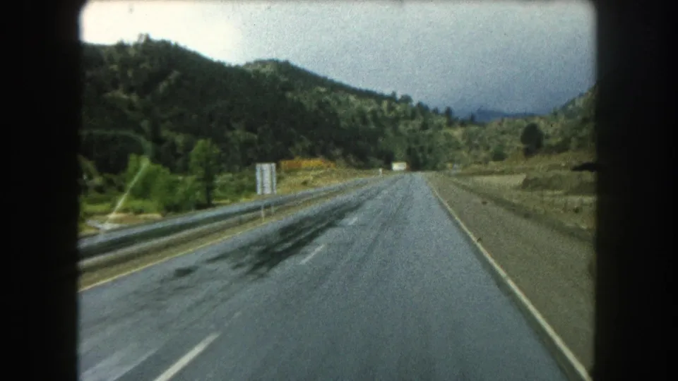 Driver’s-view 8mm frame on a wet Summit County mountain road, with guardrails and tree-covered slopes ahead.