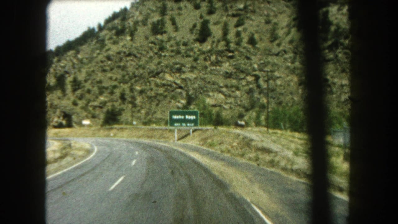 Mountain road curving toward a green Idaho Springs exit sign seen through dark car-window edges.