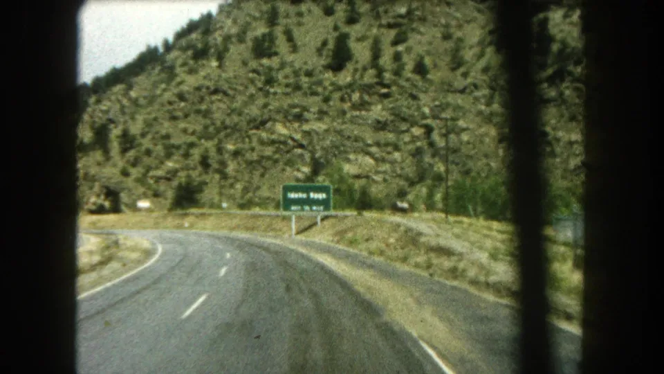 1962 8mm view from a moving car on a Colorado mountain road approaching a green Idaho Springs exit sign.