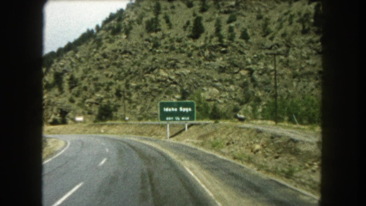 Car-window view of an Idaho Springs exit sign along a curving Colorado mountain road in the 1962 home-movie clip.