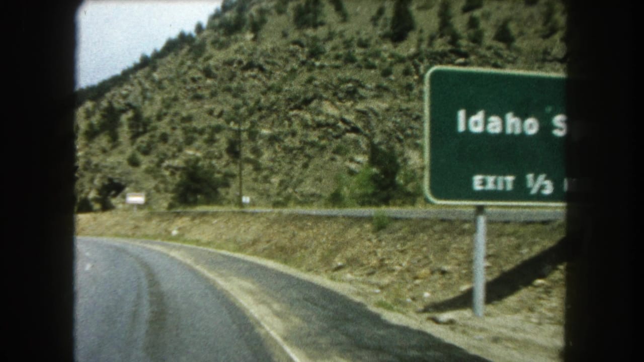 Curving mountain highway with a green Idaho Springs exit sign beside the road.