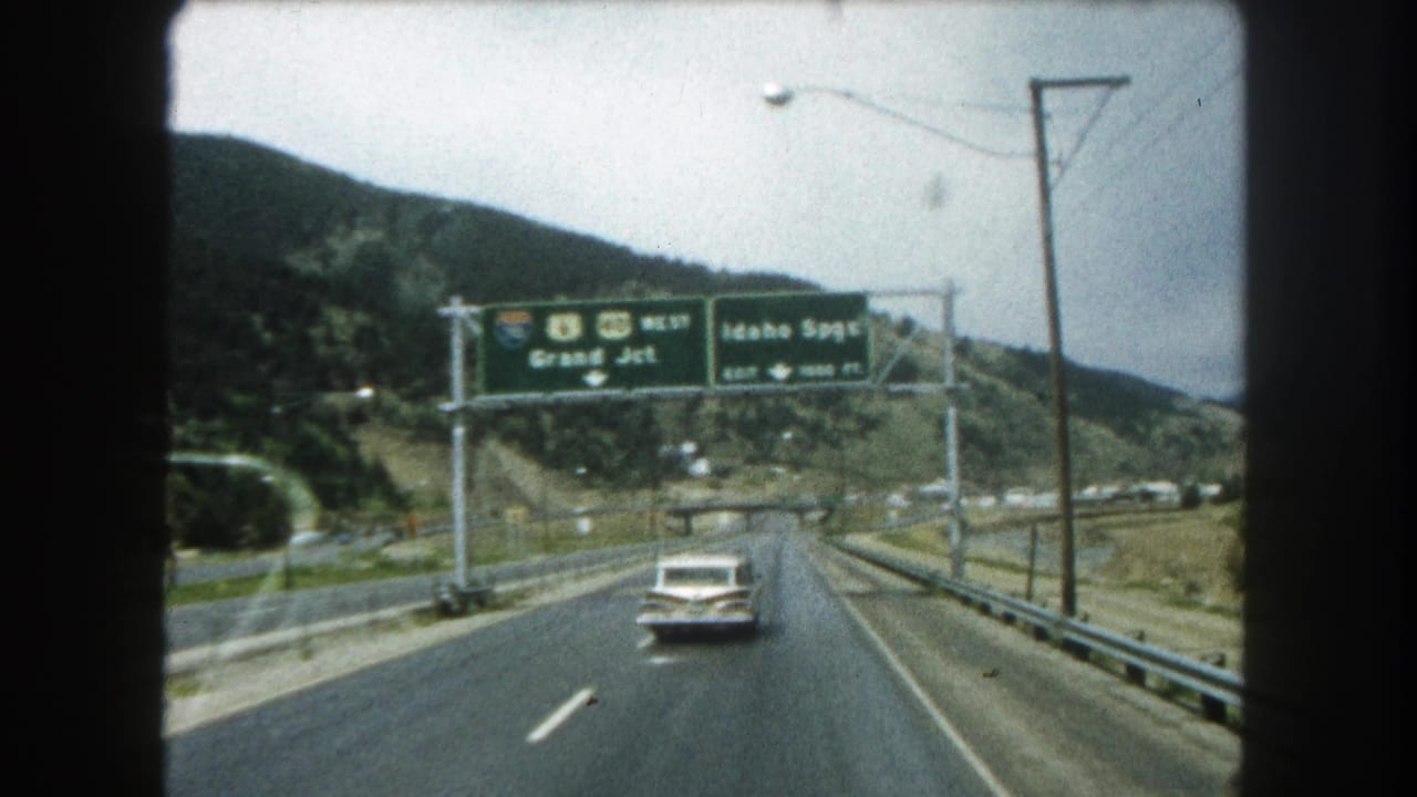 1962 8mm Colorado highway footage showing overhead signs for I-80 and U.S. 40 West, with a white sedan driving through hills.