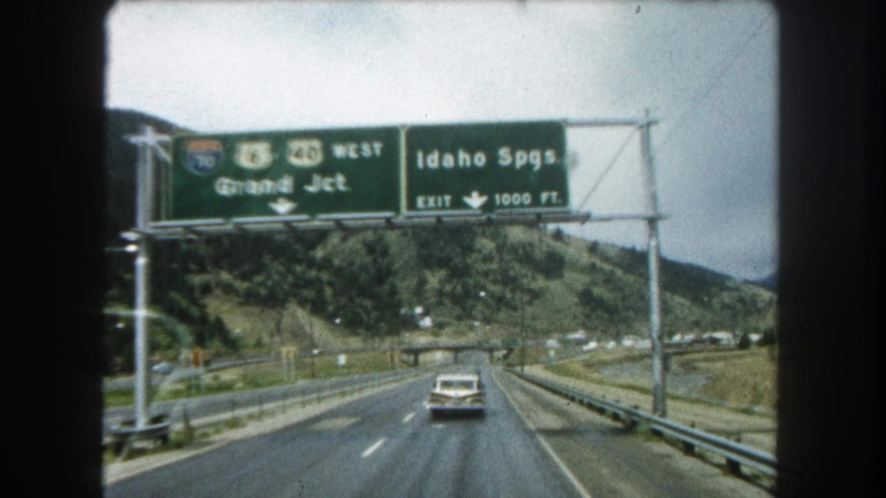 White sedan driving toward overhead signs for Grand Junction and Idaho Springs exits.