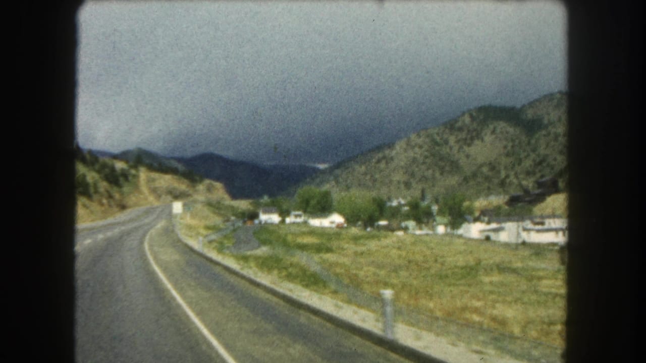 Highway shoulder and valley homes with mountains beneath a heavy cloud bank.