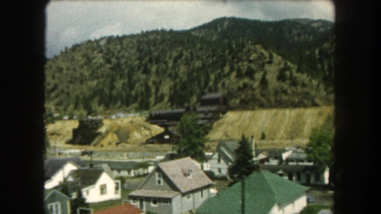 Houses at the base of a wooded hillside with dark buildings on an exposed slope.