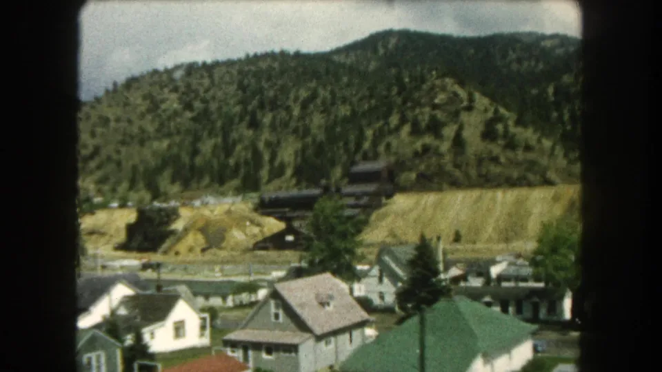 Summit County, Colorado houses and utility poles sit below a forested hillside with dark structures and exposed earth on the slope.