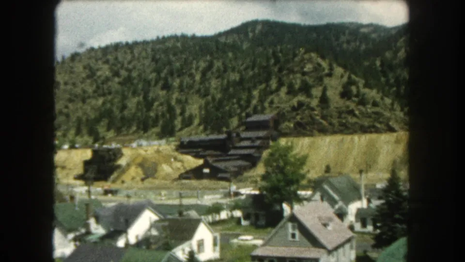 1962 mountain-town view in Summit County showing clustered homes, roadside utility poles, trees, and a hillside with exposed earth.