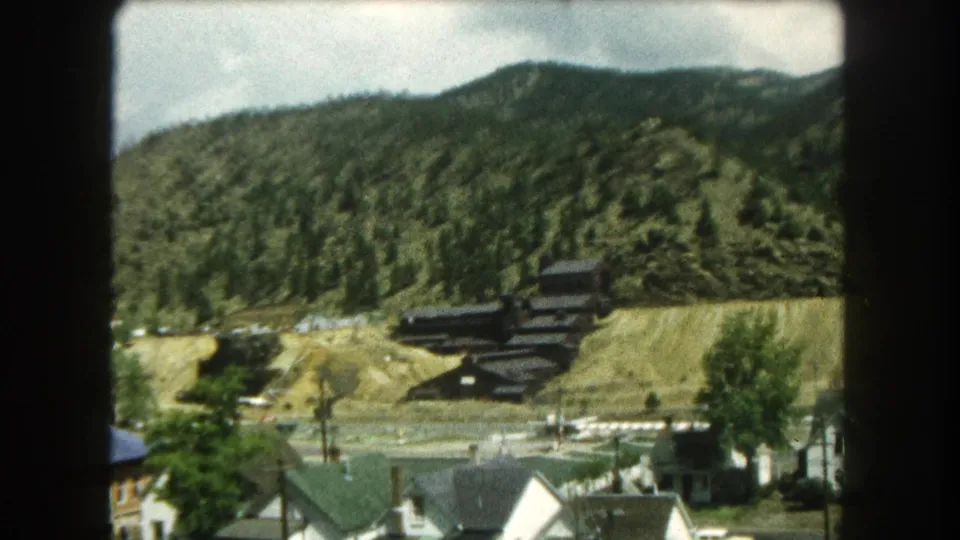 End frame of the 1962 Summit County clip with rooftops, a roadside tree, dark hillside buildings, and forested Colorado mountains.