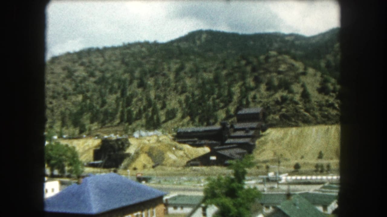 Summit County mountain-town view with a prominent blue roof, roads, and a dark structure set into a wooded hillside.