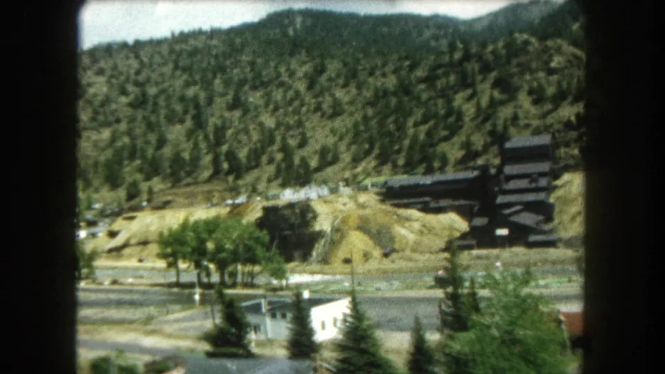 1962 8mm frame of a Summit County mountain-town overlook with houses, trees, roadways, and a hillside industrial feature.