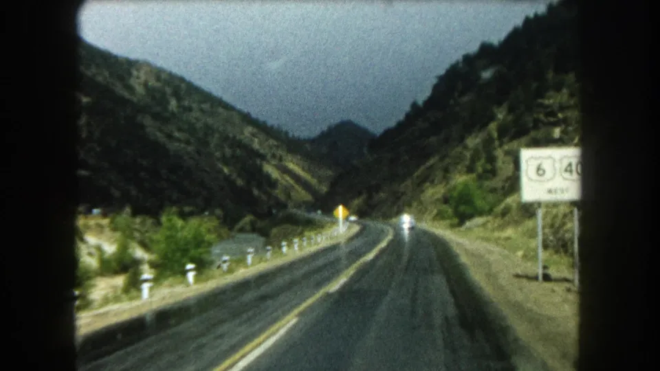 1962 Colorado road-trip frame showing a two-lane mountain road through a pass, roadside markers, vehicles, and a Route 6 sign.