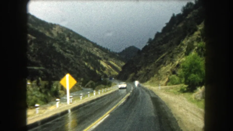 Passenger-view 8mm frame in Summit County, Colorado with a yellow warning sign, white route marker, wet road, and approaching traffic.