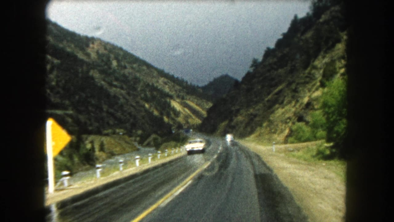 1962 Summit County, Colorado home-movie view of a wet two-lane highway through a mountain valley with an oncoming car.