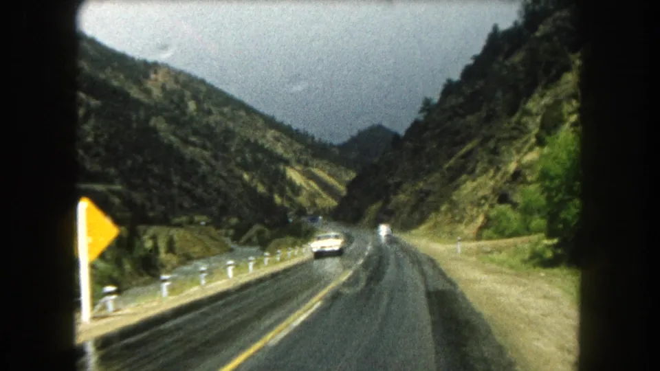1962 Summit County, Colorado home-movie view of a wet two-lane highway through a mountain valley with an oncoming car.