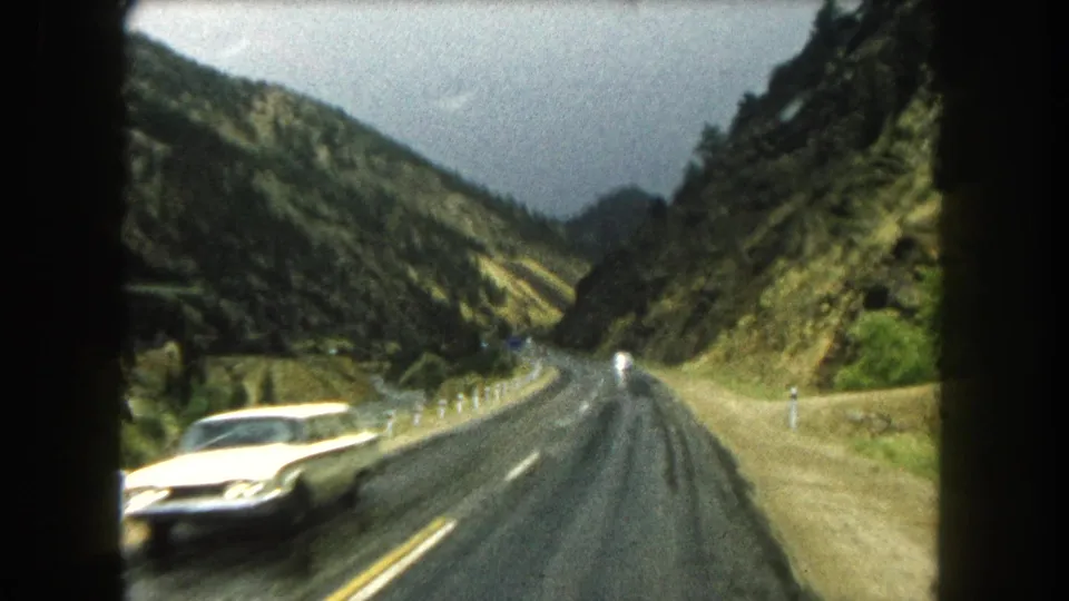 A white car passes close to the camera on a wet Summit County mountain road in 1962 home-movie footage.