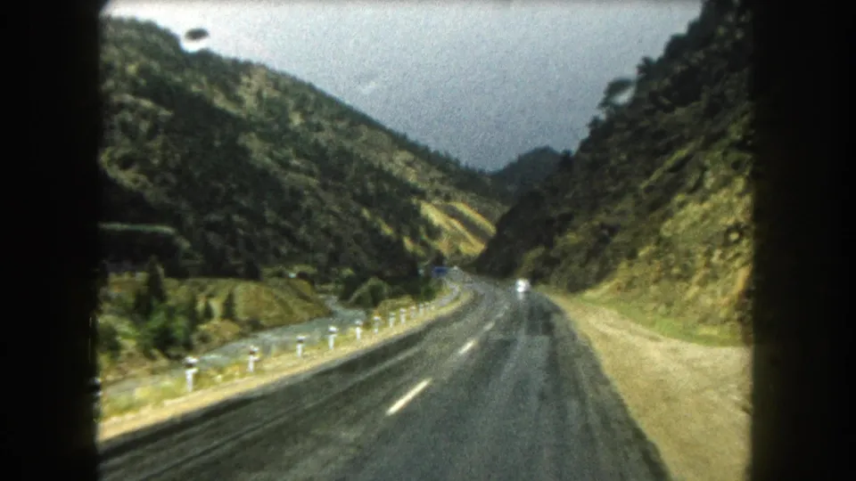 1962 Colorado mountain-road view showing a damp two-lane highway curving between forested and rocky slopes.