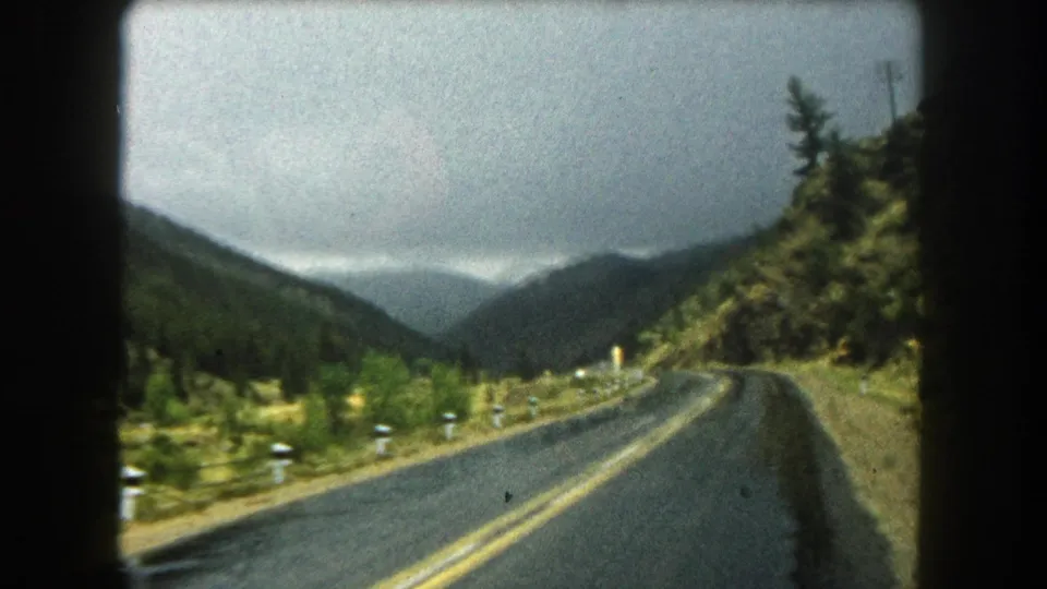 End frame of a 1962 Summit County drive, looking along a wet mountain road toward distant cloudy ridges.