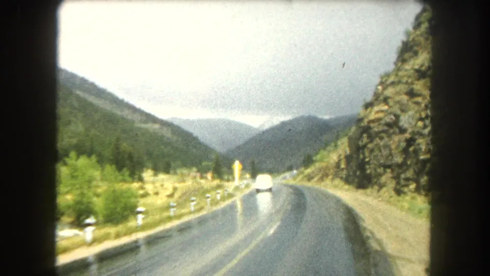 Summit County road footage shows a white car ahead on reflective pavement, framed by mountains and roadside posts.