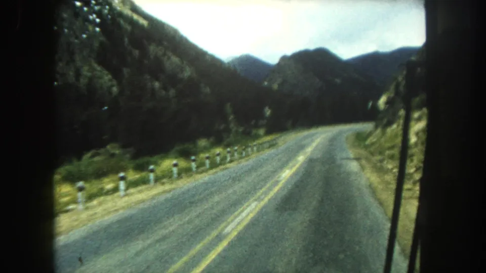 Final 8mm frame of a Summit County road bending through forested mountains, with the vehicle windshield edge at right.