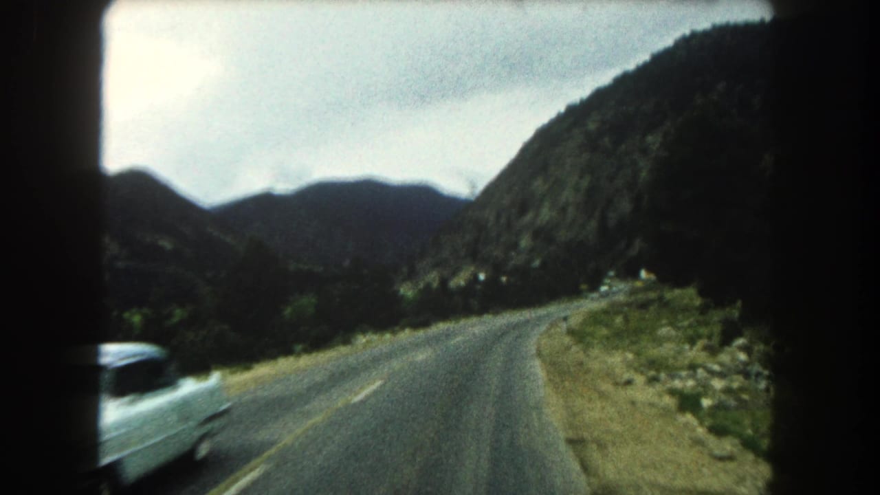 1962 Summit County road scene with a white car passing on a curved mountain highway.