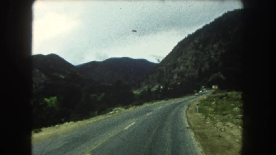 1962 8mm passenger view of a Summit County highway bending through a mountain valley.