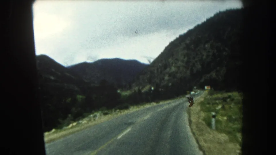 1962 Summit County mountain road view with dark ridges, roadside markers, and 8mm film borders.