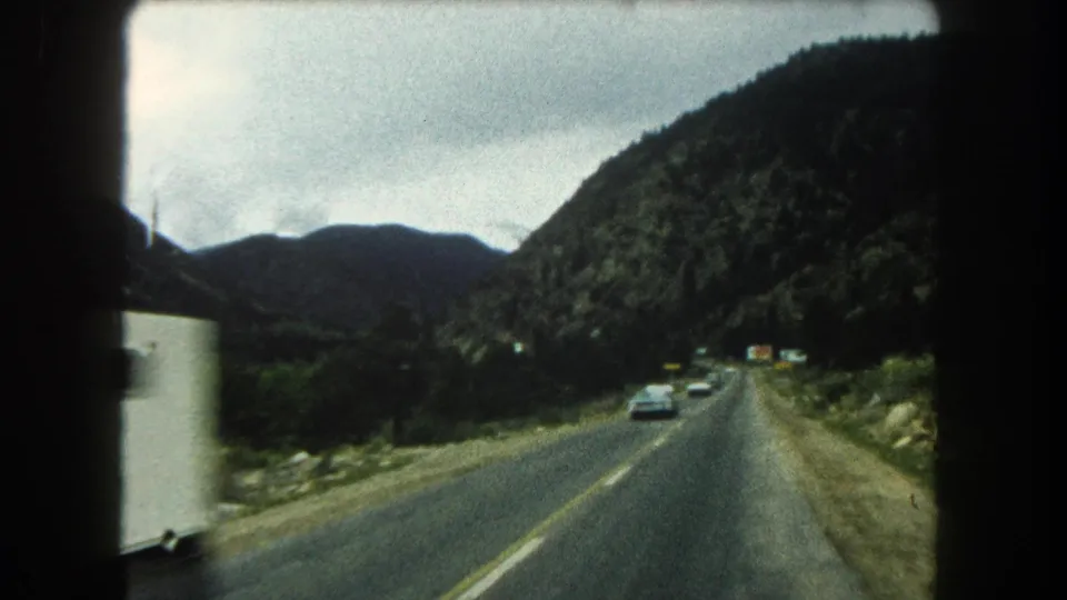1962 8mm road footage shows cars on a Summit County mountain highway with forested slopes and a valley edge beside the road.