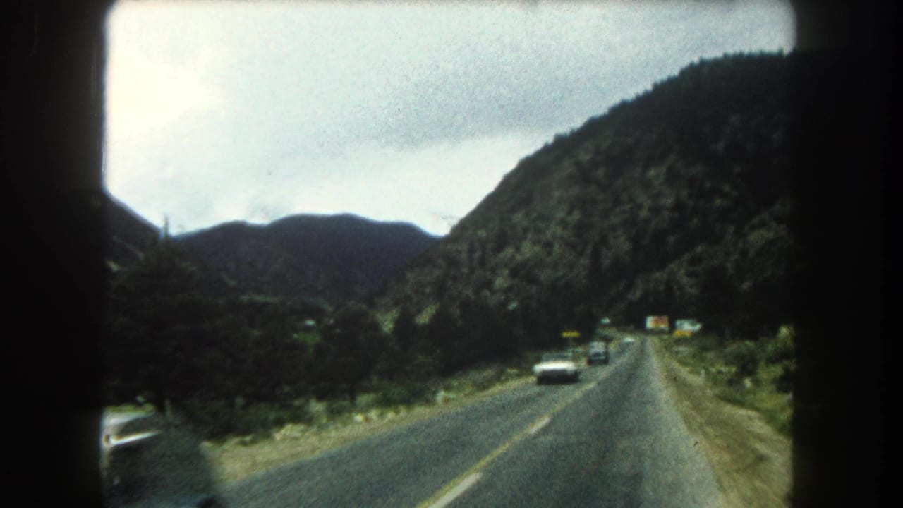 Mountain road curving through wooded hills with several cars visible ahead and opposite.