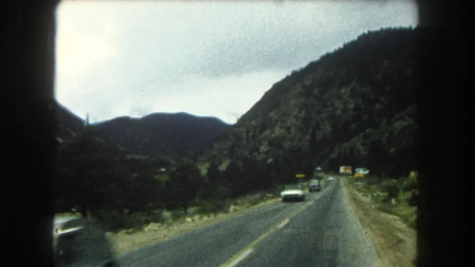 1962 Summit County, Colorado road-travel frame showing a two-lane highway through green mountain terrain with cars in view.