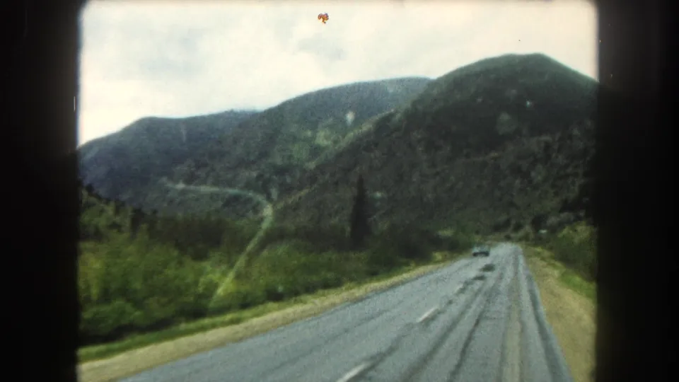 1962 8mm view of a two-lane road through Summit County mountain terrain, with wet pavement, green roadside vegetation, and film-gate borders.