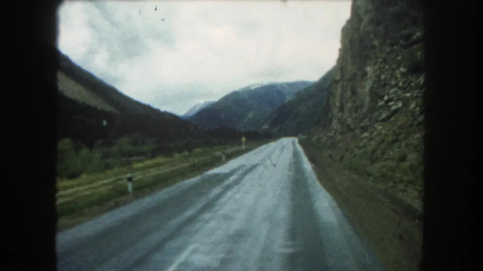 Summit County 8mm frame with a rain-darkened road, roadside markers, rocky hillside, and muted mountain backdrop.