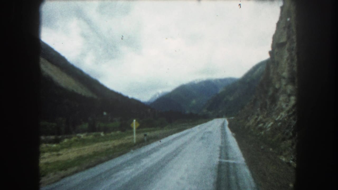 Forward 8mm view of a Summit County road through mountain terrain, with a rocky wall, valley slopes, and cloudy sky.