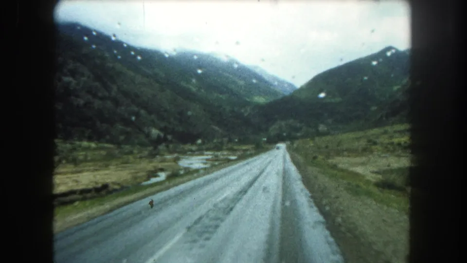 Home-movie footage from Summit County shows a rain-damp road, green hillsides, and a pale sky viewed from inside a moving vehicle.