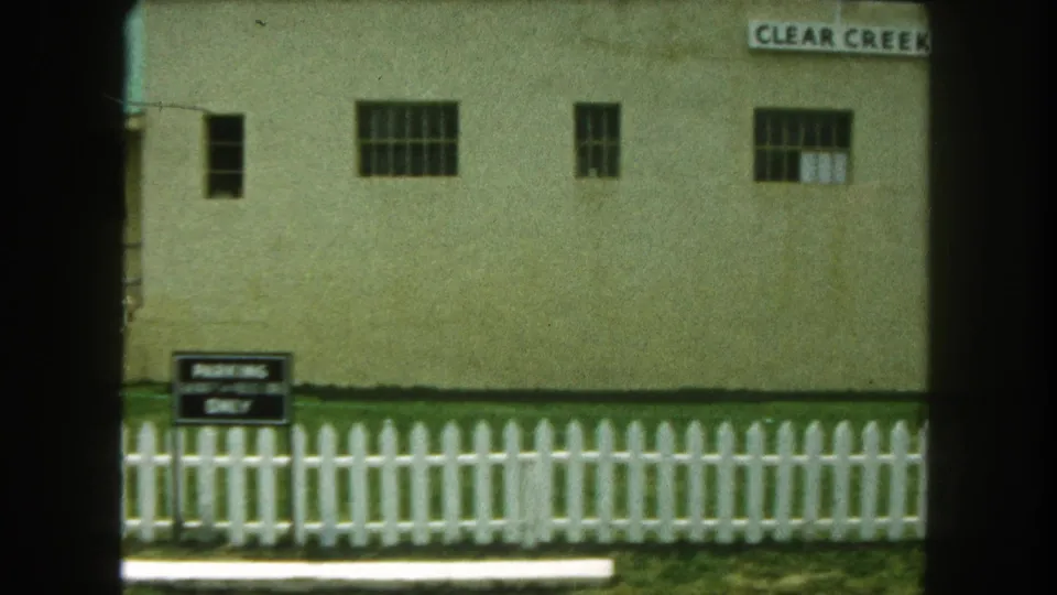 End frame of the 1962 passing view, with the jail facade, barred windows, picket fence, and small ground sign in view.