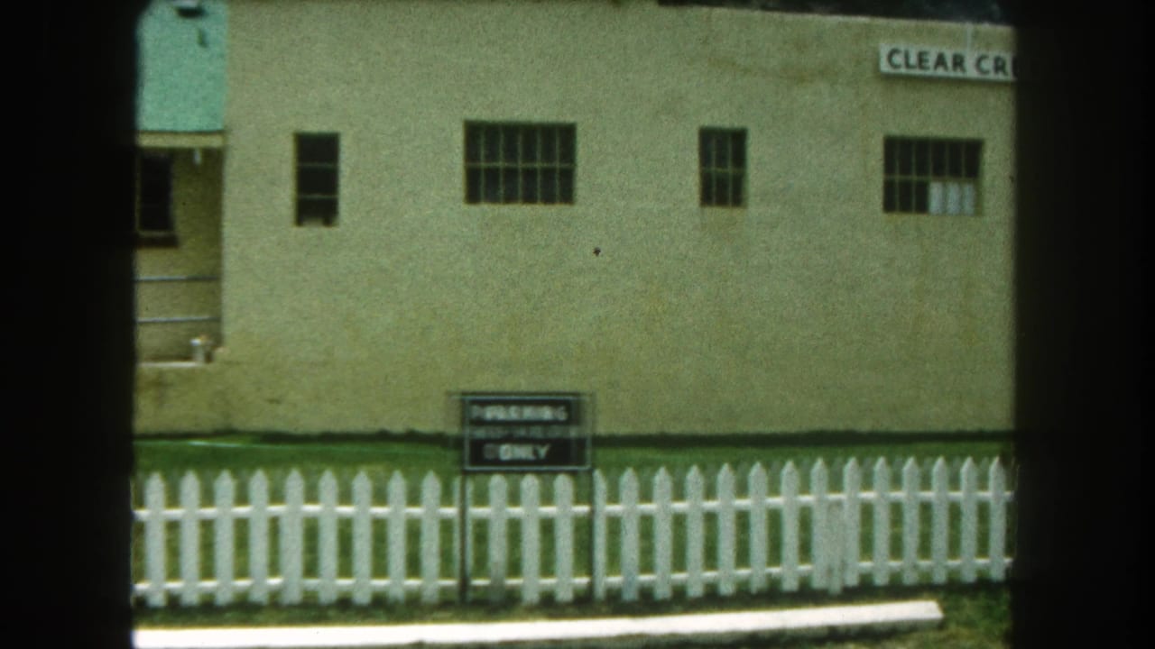 Beige building behind a white picket fence with a posted parking sign.