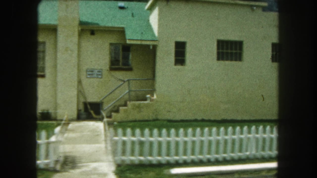 Green-roofed beige building with exterior stairs and a walkway behind a fence.