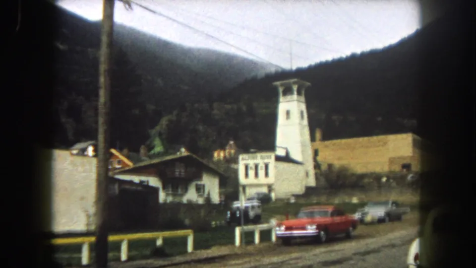 Summit County, Colorado roadside view with Alpine Hotel signage, a white tower, classic cars, utility lines, and dark forested mountains.